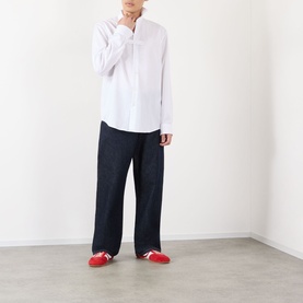 Model wearing Dries Van Noten white cotton casual shirt with band collar, styled with wide-leg dark denim trousers and red trainers.