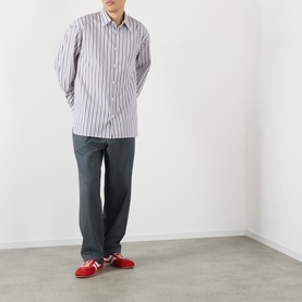 Model wearing Dries Van Noten Croom Striped Shirt in white with grey trousers and red trainers. Point collar, long sleeves, curved hem.
