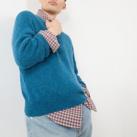 Model wearing Dries Van Noten Raf blue alpaca crew neck knit sweater, styled with a checked shirt and light blue jeans.