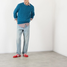Model wearing Dries Van Noten Raf blue alpaca crew neck jumper, styled with check shirt, light-wash jeans and red trainers.