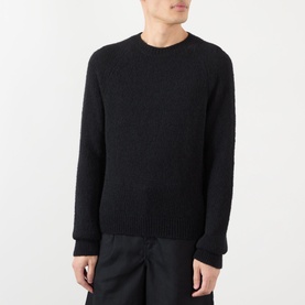 Model wearing Dries Van Noten black alpaca-wool blend crew neck jumper with ribbed cuffs and hem, paired with dark trousers.