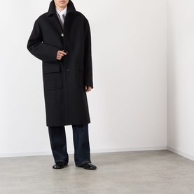 Model wearing Dries Van Noten Randale Single-Breasted Car Coat in black wool, longline silhouette with flap pockets, styled with wide-leg trousers