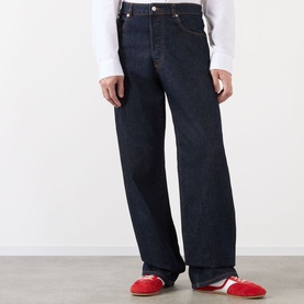 Model wearing Dries Van Noten indigo wide-leg jeans in 100% cotton, styled with a white long-sleeve top and red trainers.