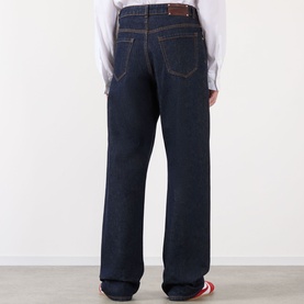 Model wearing Dries Van Noten indigo wide-leg jeans, rear view, styled with a white shirt and red trainers.