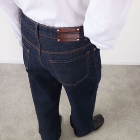 Model wearing Dries Van Noten indigo cotton jeans, rear view showing back pockets with brown leather logo patch and gold hardware.