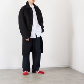 Model wearing Dries Van Noten indigo wide-leg jeans styled with a black overcoat, white shirt, and red trainers.