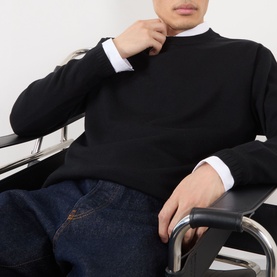 Model wearing Dries Van Noten Muchi Knit Sweater in black merino wool with crew neck and ribbed trims, styled with white shirt and blue jeans.