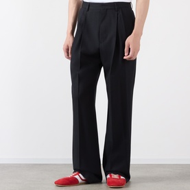 Model wearing Dries Van Noten black wool trousers with pleat front and wide leg, styled with red and white trainers.