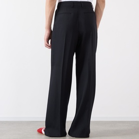 Model wearing Dries Van Noten black wide-leg wool trousers, rear view, styled with red shoes.