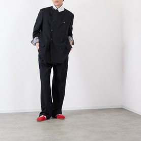 Model wearing Dries Van Noten black wool trousers with matching black jacket, white shirt, and red loafers.