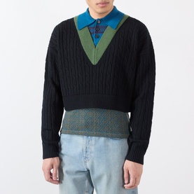 Model wearing Dries Van Noten black cable-knit wool sweater with V-neck, styled over a teal polo shirt, with light blue jeans.