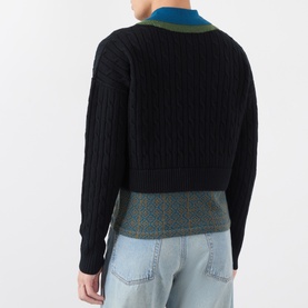 Model wearing Dries Van Noten black cable-knit wool sweater with teal contrast collar, styled with check trousers and light wash jeans, back view.