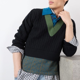 Model wearing Dries Van Noten black wool cable-knit vest over blue collar shirt, styled with patterned trousers and checked shirt layers.