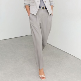 Model wearing Reiss grey tailored tapered trousers with a matching blazer, brown belt, and white heeled mules.