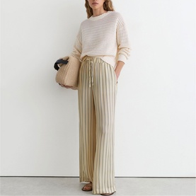 Model wearing Reiss beige striped wide-leg trousers with drawstring waist, styled with a cream knit top and carrying a tan bag.