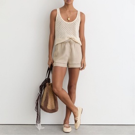 Model wearing Reiss beige linen shorts with cuffed hem, styled with cream crochet tank, woven tote bag and espadrille flats.