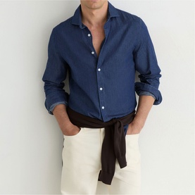 Model wearing Reiss dark blue wash linen shirt, unbuttoned at collar, styled with white trousers and dark knotted sweater at waist