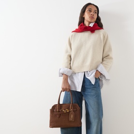 Model carrying Miu Miu Aviator Small Crossbody Bag in Rovere brown calfskin with gold-tone hardware, styled with cream knit, white shirt and jeans.