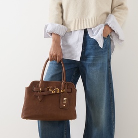 Model carrying Miu Miu Aviator Small Crossbody Bag in Rovere suede with gold-tone hardware and belt clasp, styled with jeans and cream knit