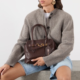 Model carrying Miu Miu Aventure Aviator Medium Bag in Radica leather with gold-tone hardware and belt clasp, styled with grey knit jacket and denim