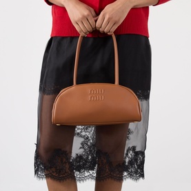Model carrying Miu Miu Beau Softy Logo Bag in cognac smooth leather with top handles and gold-toned hardware, styled with red top and black lace