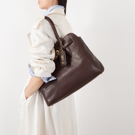 Model carrying Miu Miu Aventure Medium Leather Tote Bag in Radica with gold-tone hardware and top handles, styled with a white midi dress