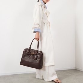 Model carrying Miu Miu Aventure Medium Leather Tote Bag in Radica with antiqued gold-tone hardware and top handles, styled with cream trench coat.