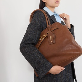 Model carrying Miu Miu Aventure Medium Leather Tote Bag in Rovere with gold-tone hardware and top handles, styled with grey blazer