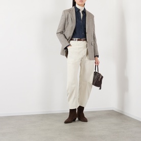 Model wearing Nili Lotan stone cotton trousers with a grey blazer, navy shirt, brown ankle boots, and carrying a small dark bag.