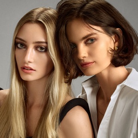 Two models with styled hair &mdash; one long blonde, one short brunette &mdash; showcasing results of Oribe Gold Lust Dry Heat Protection Spray