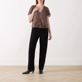 Model wearing Paige Dark Brown Multi silk blouse with flutter sleeves and V-neck, styled with black straight-leg trousers and heeled boots.