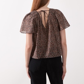 Model wearing Paige dark brown multi silk blouse, back view showing V-neckline with tie detail and flutter sleeves, styled with black trousers