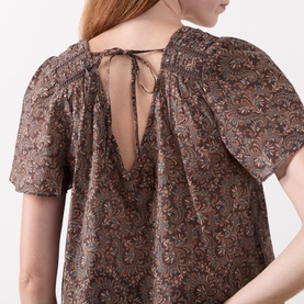 Model wearing Paige Dark Brown Multi silk blouse, back view showing V-neckline with tie detail, puff sleeves and floral paisley print.