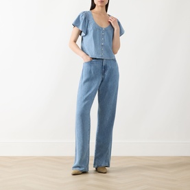 Model wearing Paige top in Palos Verdes blue denim, short flutter sleeves, button-front detail, styled with wide-leg denim trousers.