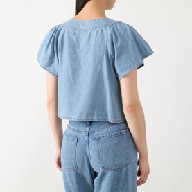 Model wearing Paige top in Palos Verdes blue denim, flutter sleeves, cropped silhouette, styled with light wash wide-leg jeans. Back view.