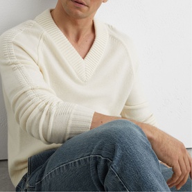 Model wearing cream V-neck ribbed knit sweater, styled with Reiss Vintage Blue Wash jeans, seated against a light wall.