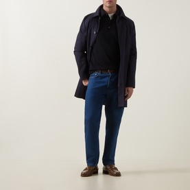 Model wearing Tiger of Sweden Night Sky wool polo with navy overcoat, blue jeans, and brown leather loafers