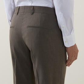 Model wearing Tiger of Sweden stone suit trousers, rear view showing back pockets, styled with a white dress shirt.