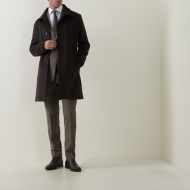 Model wearing Tiger of Sweden stone suit trousers, styled with a dark overcoat, tie, and black leather shoes.