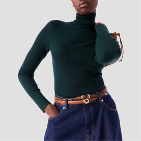 Model wearing Maje dark green ribbed turtleneck long-sleeve top, styled with blue denim jeans and tan leather belt