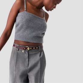 Model wearing Maje gold-tone belt with disc eyelets in brown leather, styled with grey knit crop top and tailored trousers