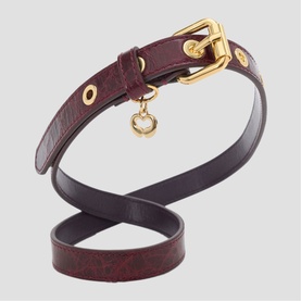 Maje gold-tone buckle belt in dark burgundy leather with eyelet detailing and small charm pendant.