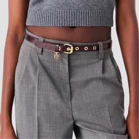 Model wearing Maje gold-tone belt in dark burgundy croc-effect leather with gold disc charm, styled with grey tailored trousers and crop knit top