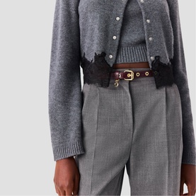 Model wearing Maje gold-tone belt with brown leather strap, styled with grey knit cardigan and tailored grey trousers.