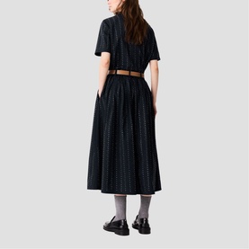 Model wearing Maje Womens French Dress in black with allover dot pattern, short sleeves, pleated midi skirt, styled with tan belt and black loafers