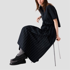 Model wearing Maje Womens French Dress in black with subtle pinstripe detail, styled with black loafers, seated pose
