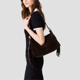 Model carrying Maje dark brown suede hobo bag with fringe tassel detail and gold-tone zip, worn over shoulder, styled with black dress