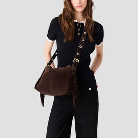 Model carrying Maje dark brown suede shoulder bag with gold buckle hardware, fringe detail, and adjustable strap, styled with black outfit
