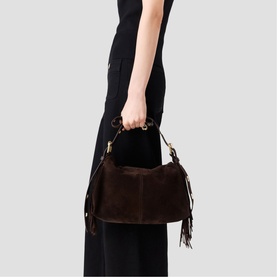 Model carrying Maje dark brown suede bag with fringe detail, gold-tone hardware, and top handle, styled with black wide-leg trousers