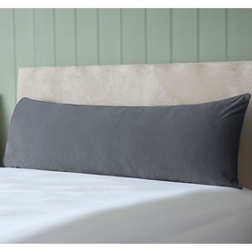 Belledorm Velvet Bolster Cushion in charcoal, long rectangular shape, styled on a bed with white bedding against a sage green panelled headboard